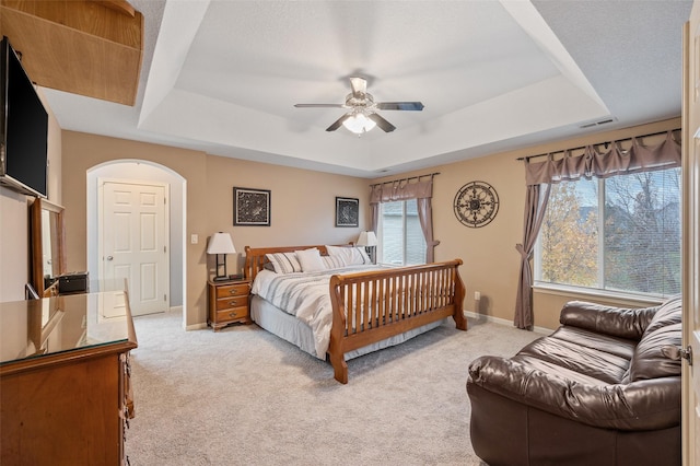 carpeted bedroom with ceiling fan and a raised ceiling