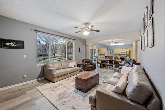 living room with ceiling fan, light wood-type flooring, decorative columns, and a textured ceiling