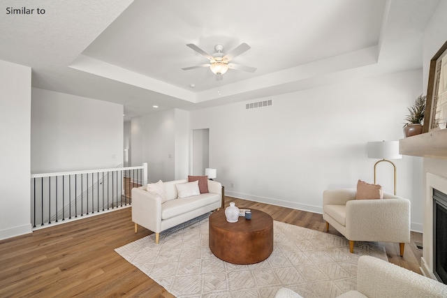 living room featuring a tray ceiling, ceiling fan, and light hardwood / wood-style flooring