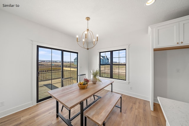 dining space featuring a textured ceiling, light hardwood / wood-style floors, and a notable chandelier