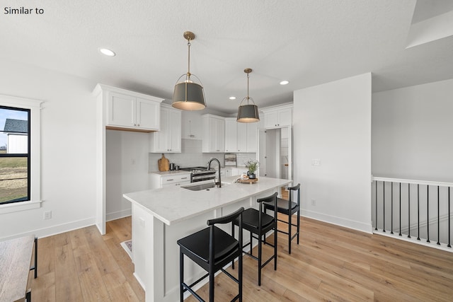 kitchen with white cabinetry, sink, hanging light fixtures, a kitchen island with sink, and light wood-type flooring