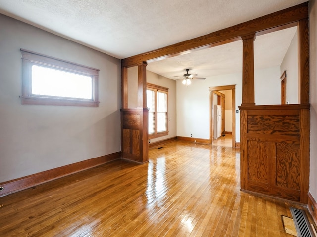 empty room with ceiling fan, decorative columns, a textured ceiling, and light hardwood / wood-style flooring