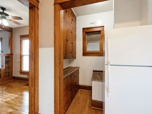 kitchen with wood walls, ceiling fan, white refrigerator, and light hardwood / wood-style flooring