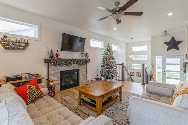 living room with ceiling fan with notable chandelier, light hardwood / wood-style flooring, and a stone fireplace