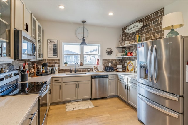 kitchen featuring sink, tasteful backsplash, hanging light fixtures, light hardwood / wood-style flooring, and stainless steel appliances