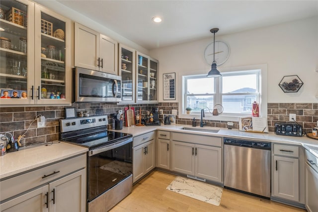 kitchen featuring sink, backsplash, stainless steel appliances, light hardwood / wood-style floors, and decorative light fixtures