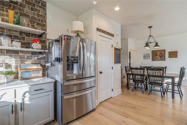 kitchen with gray cabinetry, light hardwood / wood-style flooring, hanging light fixtures, stainless steel fridge, and backsplash