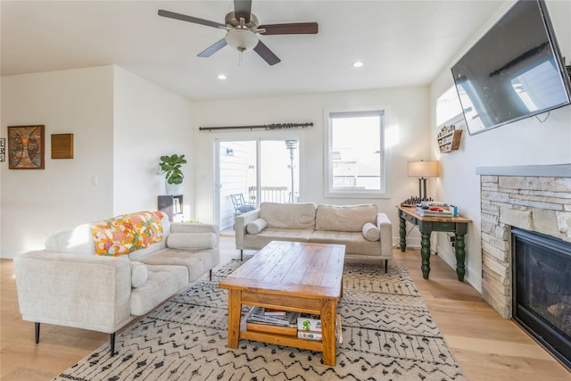 living room featuring ceiling fan, a stone fireplace, and light hardwood / wood-style floors