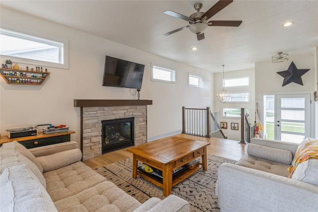 living room featuring a stone fireplace, ceiling fan with notable chandelier, and light wood-type flooring