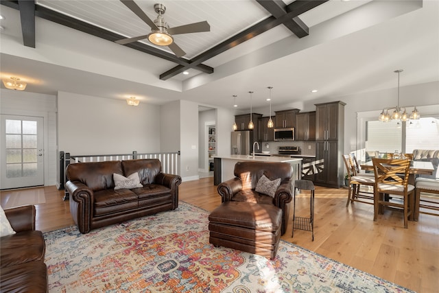 living room with beamed ceiling, ceiling fan with notable chandelier, sink, and light hardwood / wood-style flooring