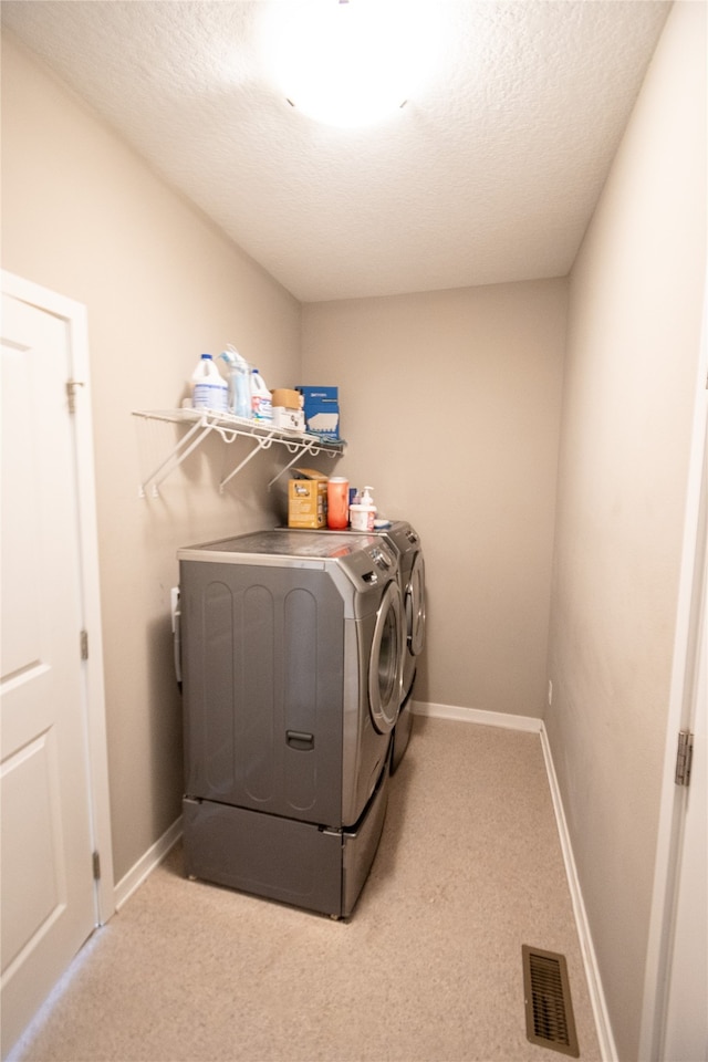 clothes washing area featuring light carpet, a textured ceiling, and washing machine and clothes dryer