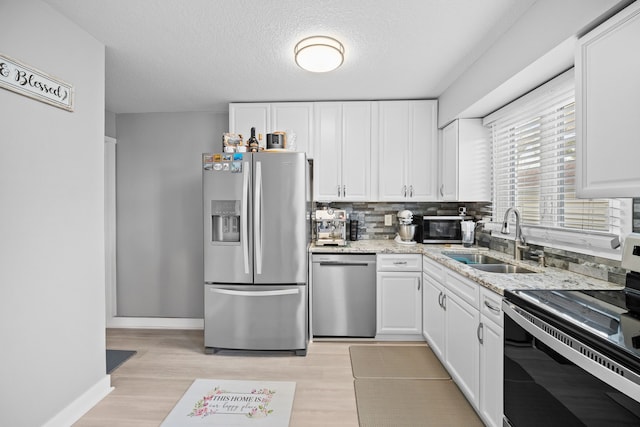 kitchen with sink, light hardwood / wood-style floors, light stone counters, white cabinetry, and stainless steel appliances