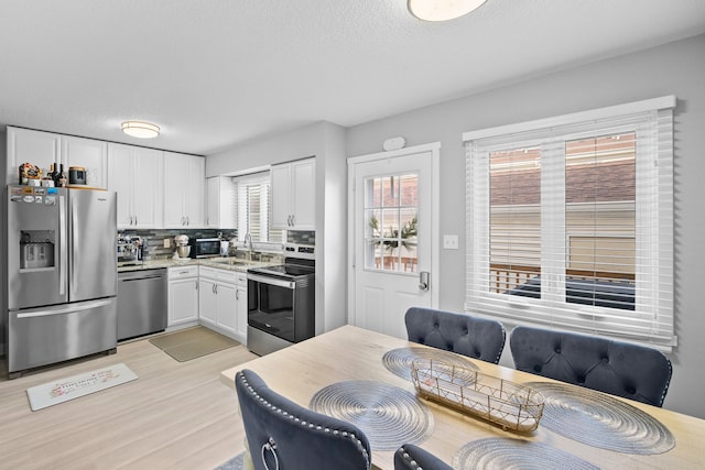 kitchen with appliances with stainless steel finishes, backsplash, sink, light hardwood / wood-style flooring, and white cabinetry