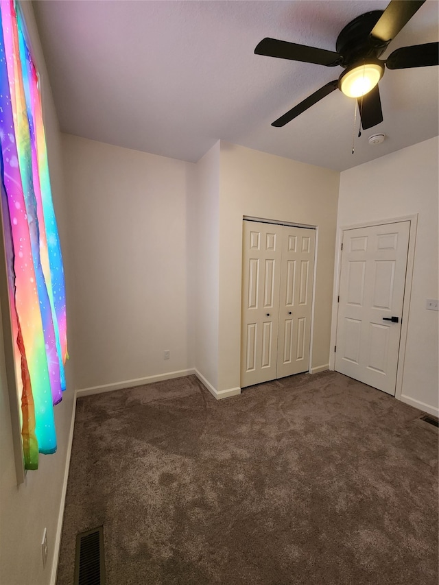 unfurnished bedroom with dark colored carpet, ceiling fan, and a closet