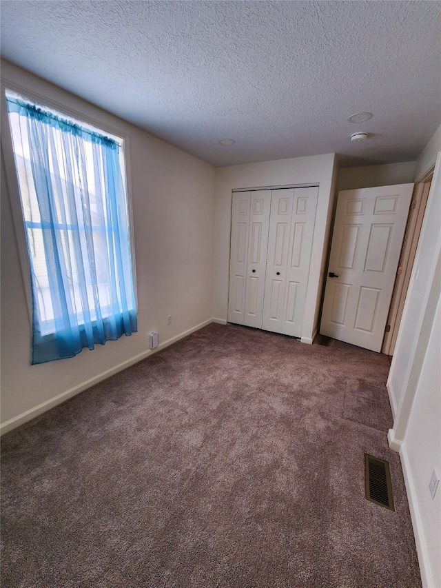 unfurnished bedroom with dark carpet, a textured ceiling, and a closet