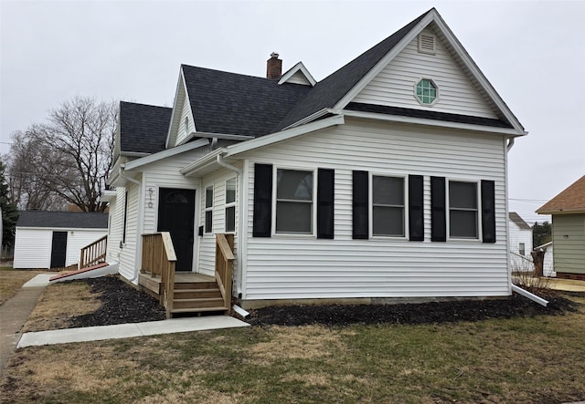 view of front of house with a chimney, a shingled roof, a front lawn, and an outdoor structure