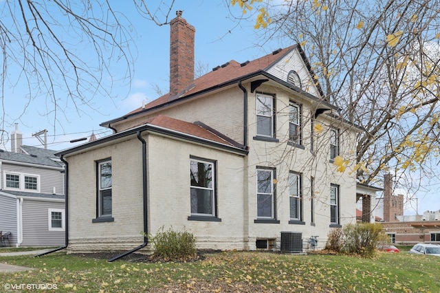 view of side of property with a chimney, central AC unit, a lawn, and brick siding