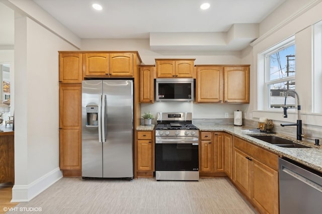 kitchen featuring stainless steel appliances, recessed lighting, brown cabinetry, a sink, and light stone countertops