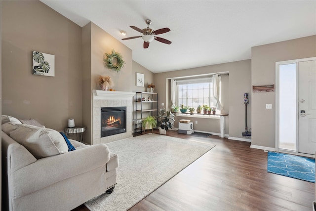 living room featuring dark hardwood / wood-style floors, high vaulted ceiling, ceiling fan, and a tiled fireplace