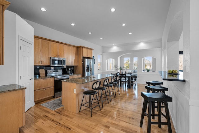 kitchen featuring a breakfast bar area, dark stone counters, stainless steel appliances, and light hardwood / wood-style floors