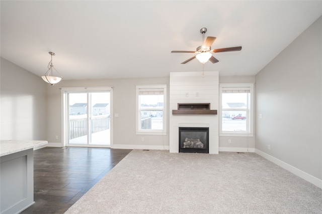 unfurnished living room featuring a fireplace, dark wood-type flooring, ceiling fan, and a healthy amount of sunlight