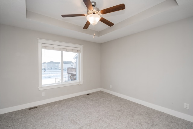 carpeted spare room with a tray ceiling and ceiling fan