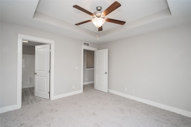 unfurnished bedroom with ceiling fan, a raised ceiling, and light carpet