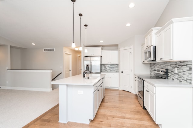 kitchen with light wood-type flooring, stainless steel appliances, decorative light fixtures, a center island with sink, and white cabinetry