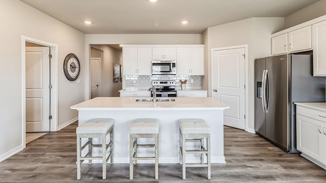 kitchen featuring white cabinetry, a center island with sink, stainless steel appliances, tasteful backsplash, and a breakfast bar