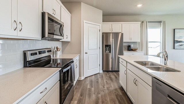 kitchen with light stone counters, appliances with stainless steel finishes, white cabinets, a sink, and wood finished floors