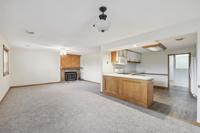 kitchen featuring ceiling fan, light hardwood / wood-style flooring, kitchen peninsula, white appliances, and a fireplace