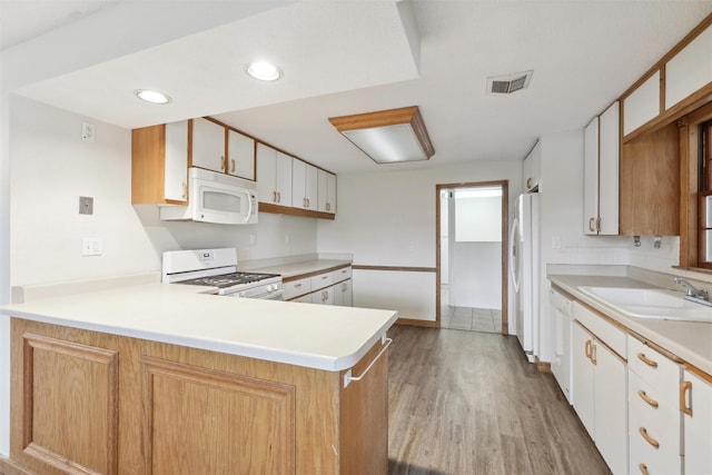 kitchen with kitchen peninsula, white appliances, sink, light hardwood / wood-style flooring, and white cabinets