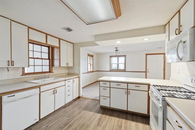 kitchen with kitchen peninsula, white appliances, sink, white cabinets, and light hardwood / wood-style floors