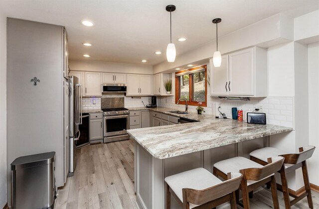 kitchen with pendant lighting, high quality appliances, sink, kitchen peninsula, and light stone countertops