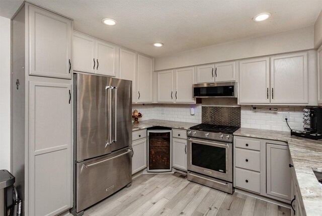 kitchen featuring wine cooler, tasteful backsplash, light hardwood / wood-style flooring, stainless steel appliances, and light stone countertops