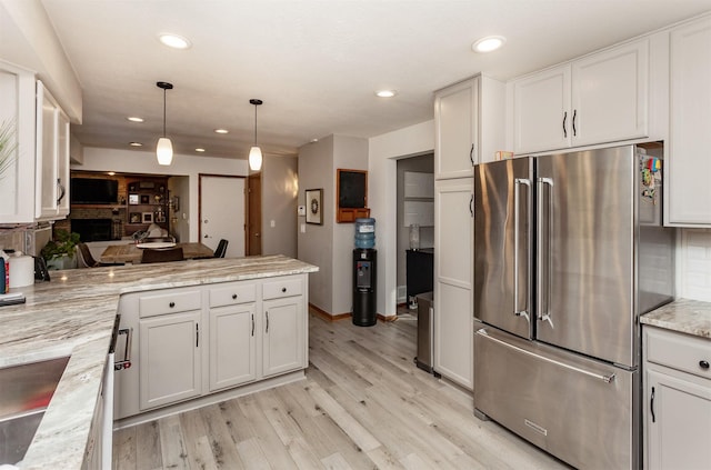 kitchen with hanging light fixtures, high end fridge, light stone countertops, light hardwood / wood-style floors, and white cabinetry