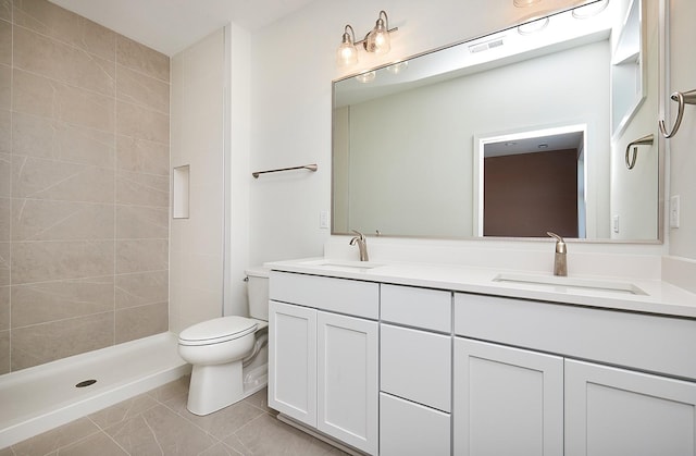 bathroom with toilet, vanity, tiled shower, and tile patterned floors