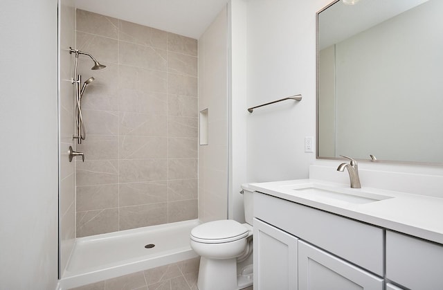 bathroom featuring tile patterned flooring, a tile shower, vanity, and toilet