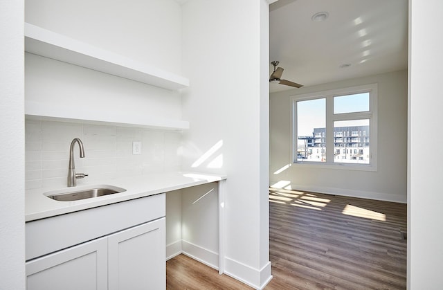 bar featuring backsplash, ceiling fan, sink, hardwood / wood-style flooring, and white cabinetry