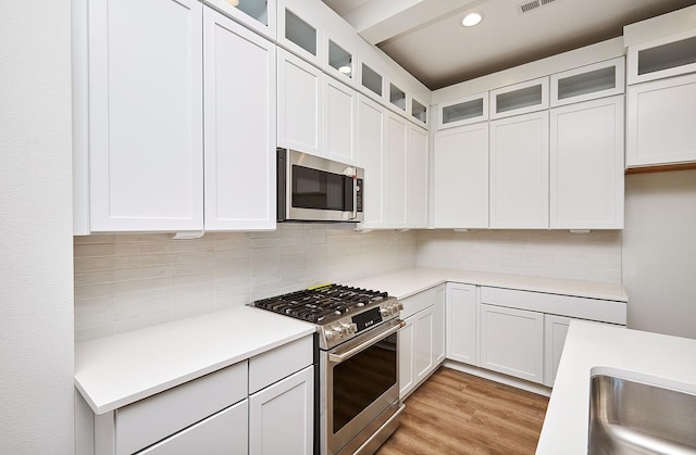 kitchen with white cabinets, tasteful backsplash, appliances with stainless steel finishes, and light hardwood / wood-style flooring