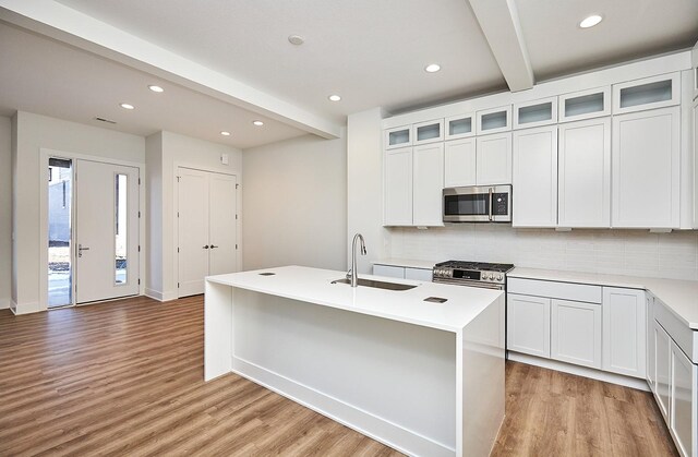 kitchen with appliances with stainless steel finishes, sink, a center island with sink, beamed ceiling, and white cabinetry