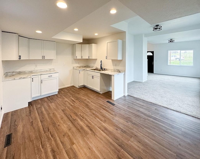 kitchen with light stone counters, light hardwood / wood-style floors, white cabinetry, and sink