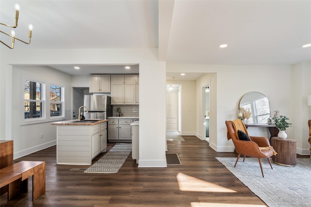 kitchen with backsplash, dark wood-type flooring, sink, stainless steel fridge, and a chandelier