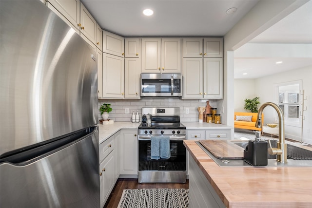 kitchen featuring sink, dark hardwood / wood-style flooring, butcher block countertops, decorative backsplash, and appliances with stainless steel finishes