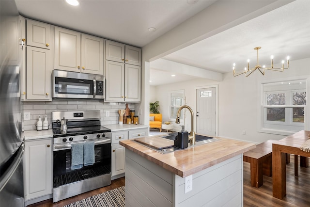 kitchen featuring backsplash, stainless steel appliances, a kitchen island with sink, dark hardwood / wood-style floors, and butcher block counters