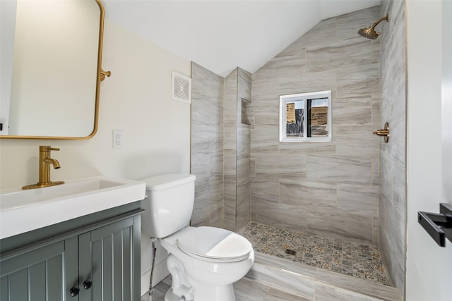 bathroom featuring a tile shower, vanity, lofted ceiling, and toilet