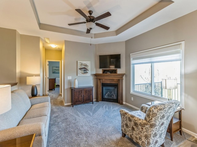 carpeted living room with ceiling fan and a tray ceiling