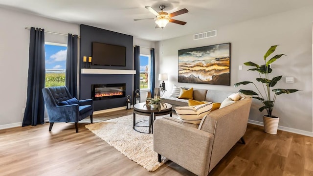 living room featuring hardwood / wood-style flooring, ceiling fan, and a large fireplace