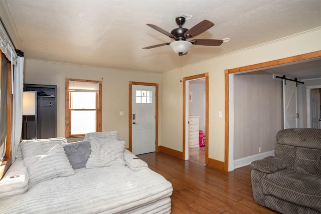 bedroom with dark hardwood / wood-style floors, ceiling fan, a barn door, and ornamental molding