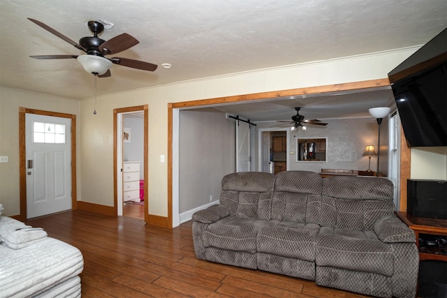 living room featuring dark hardwood / wood-style flooring, a barn door, ceiling fan, and crown molding